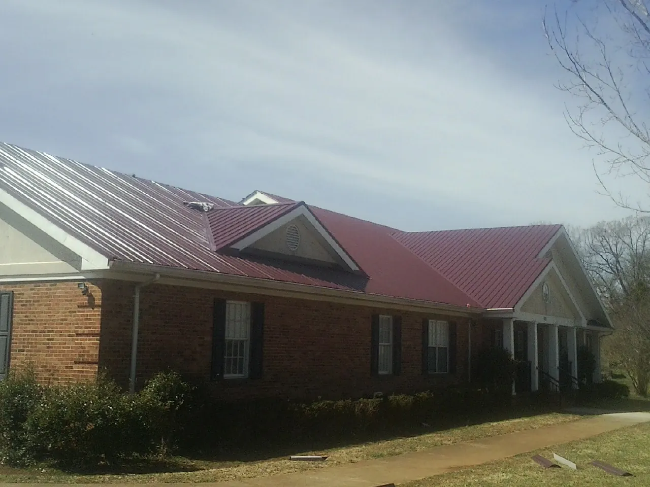 Red metal roof with gabled entries on a long brick building, from a Hail Damage Roof Repair job in Beaverton