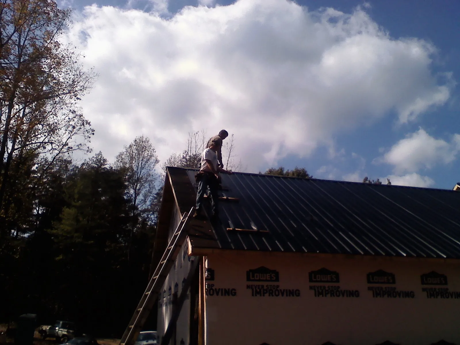 Roofer fastening dark metal panels high against a cloudy sky, from a Roof Inspection job in Beaverton