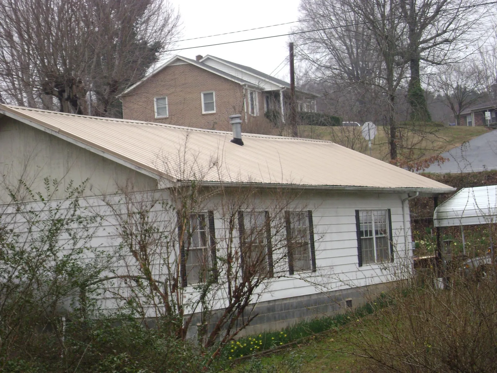 Tan metal roof on a white sided house set into a hillside — Commercial Roofing by Roofing Brothers in Beaverton